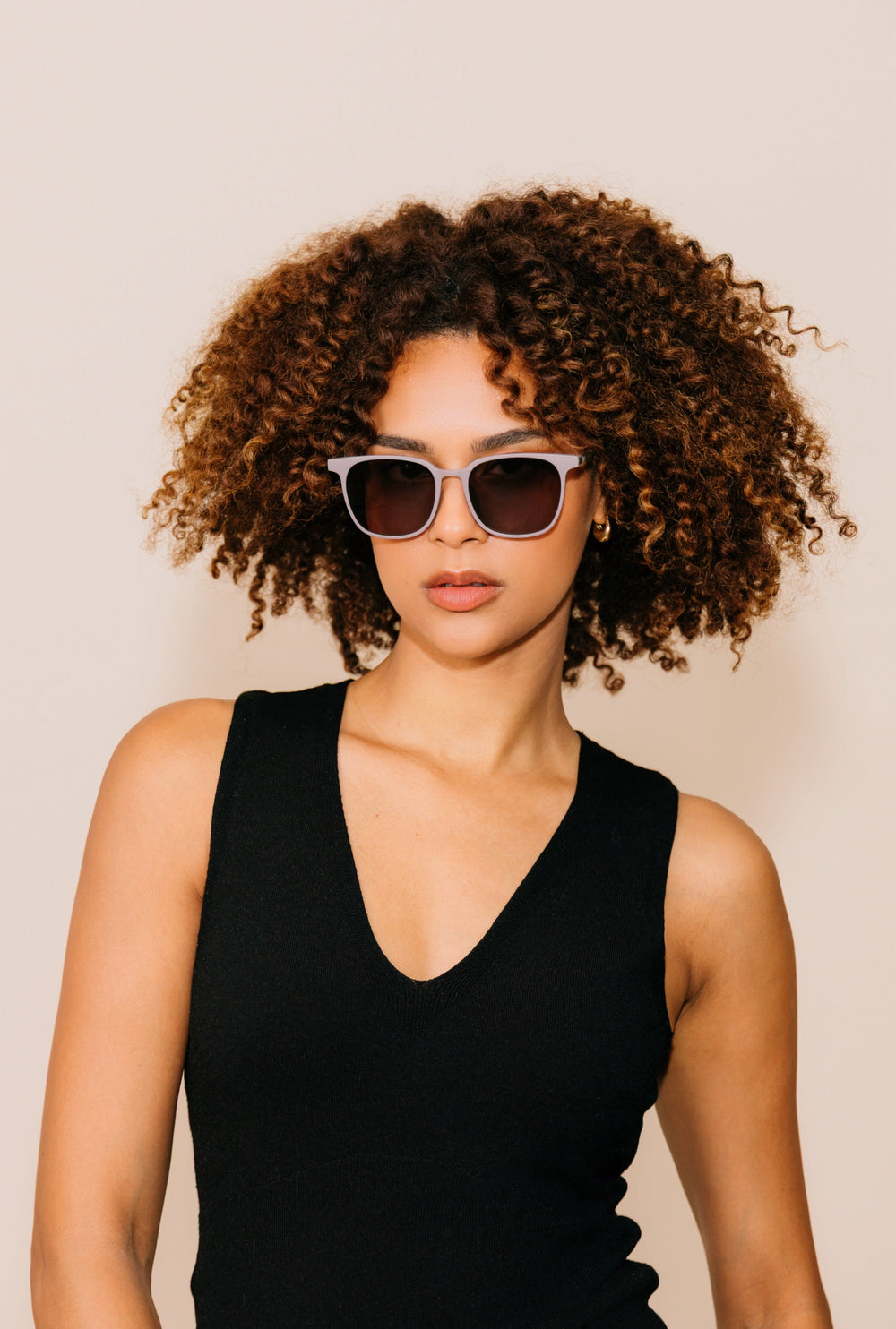 Woman wearing sunglasses and a black sleeveless top against a beige background