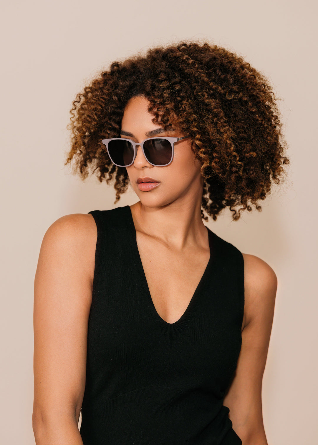 Woman wearing sunglasses and a black sleeveless top against a beige background