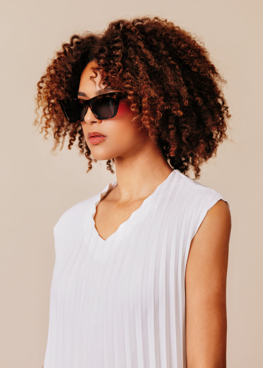 Woman wearing sunglasses and a white sleeveless top against a beige background