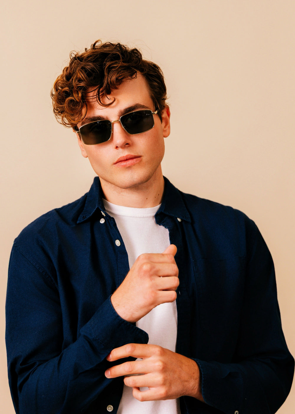 Man wearing sunglasses and a dark jacket against a beige background