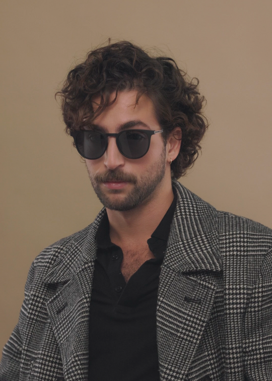 Male model wearing Altair matte black titanium prescription sunglasses, styled in a modern outfit.