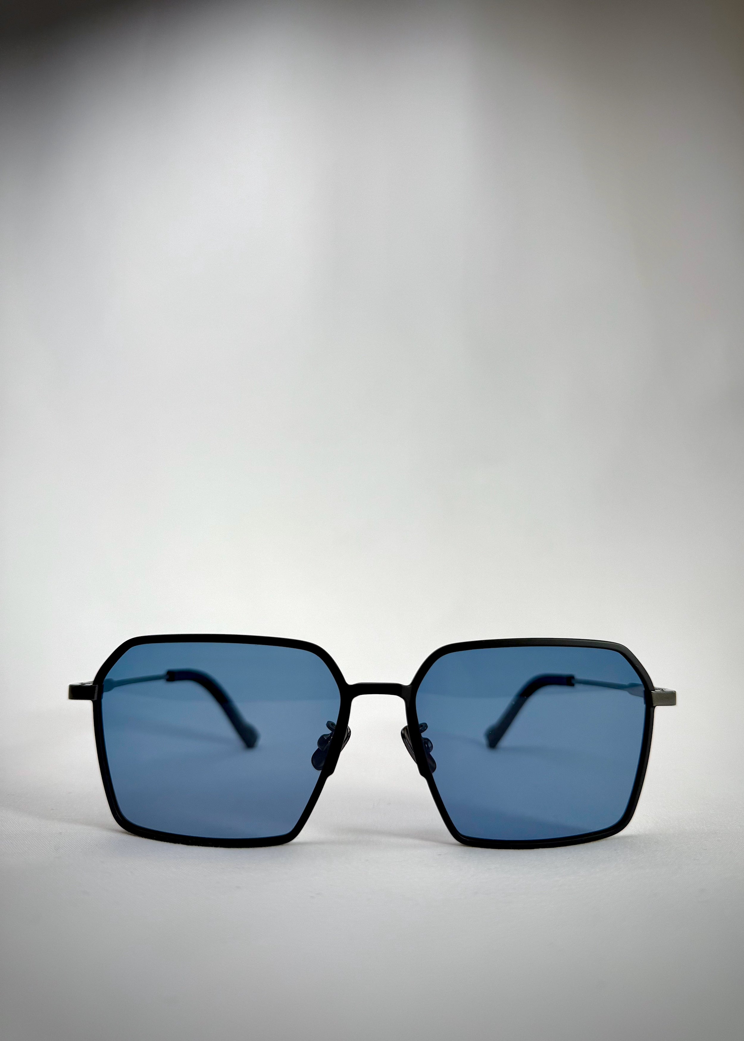 Front view of Rigel matte black titanium prescription sunglasses with a bold square frame and blue-tinted polarized lenses.