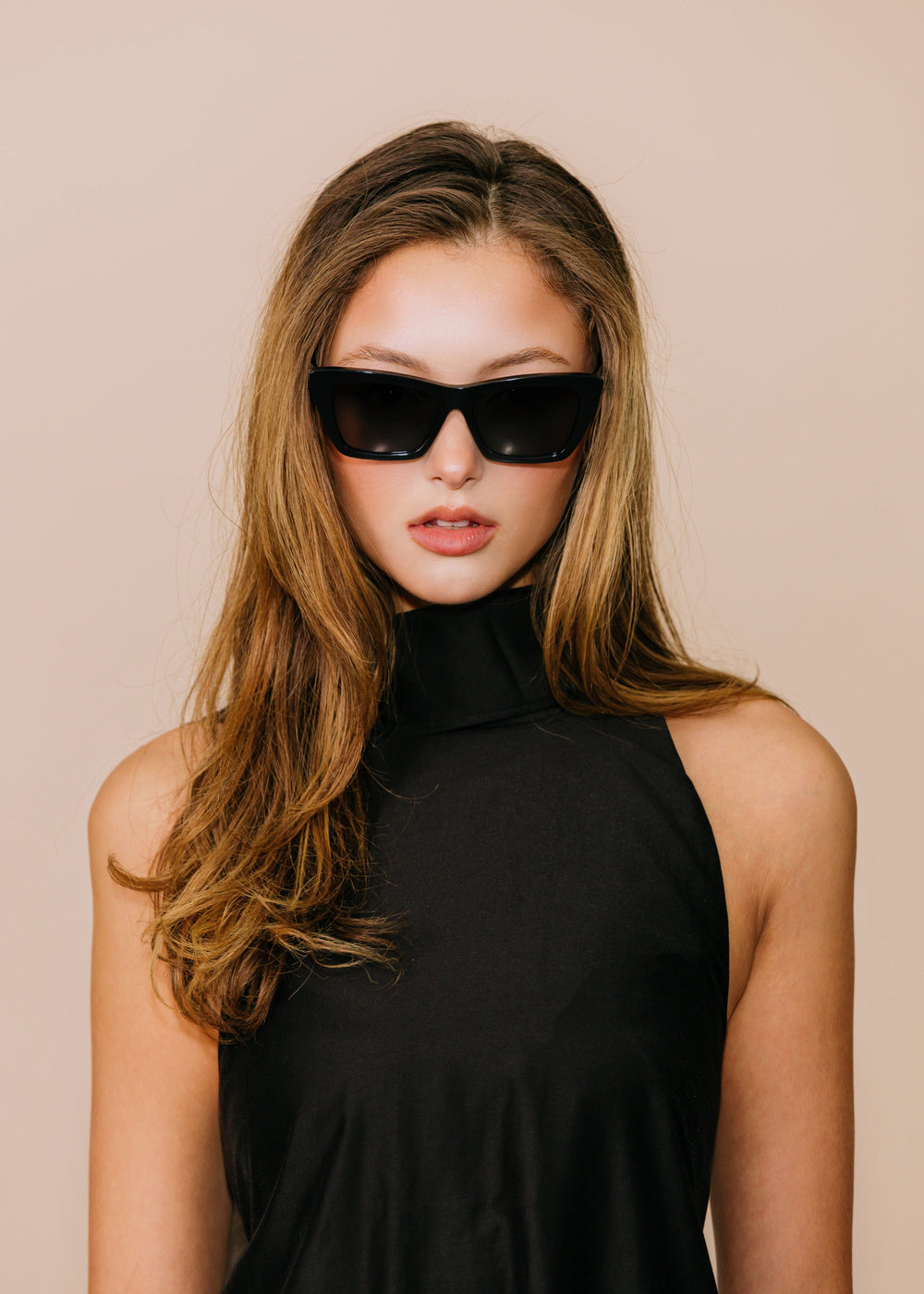 Female model wearing Aquila Black sunglasses with a black sleeveless high-neck top, facing forward.
