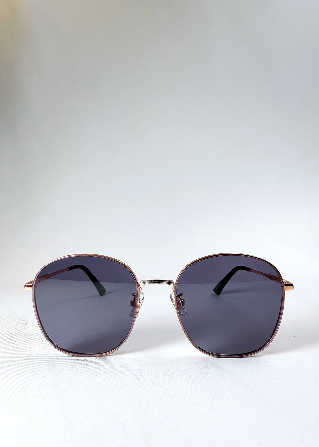 Astris Midnight Blue sunglasses – front view showing full navy lenses and rose gold geometric frame. 