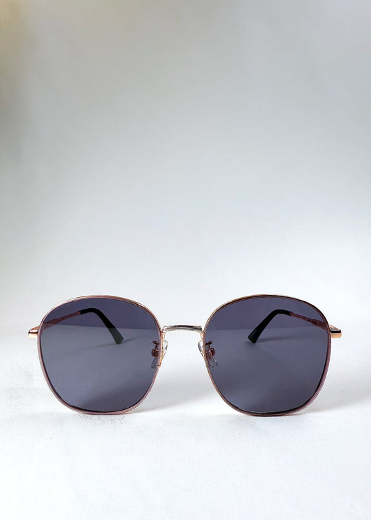 Astris Midnight Blue sunglasses – front view showing full navy lenses and rose gold geometric frame. 