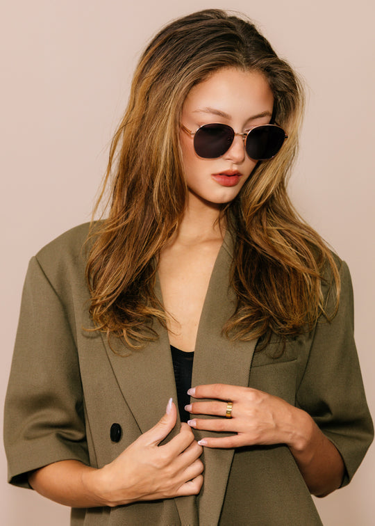 Woman wearing a green blazer and sunglasses against a beige background