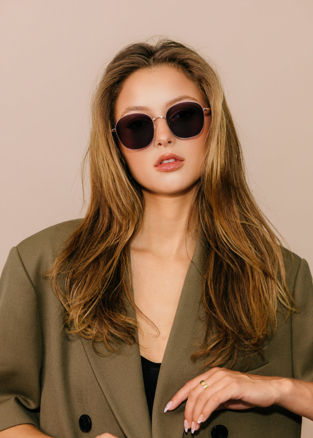 Woman wearing sunglasses and a green blazer against a beige background