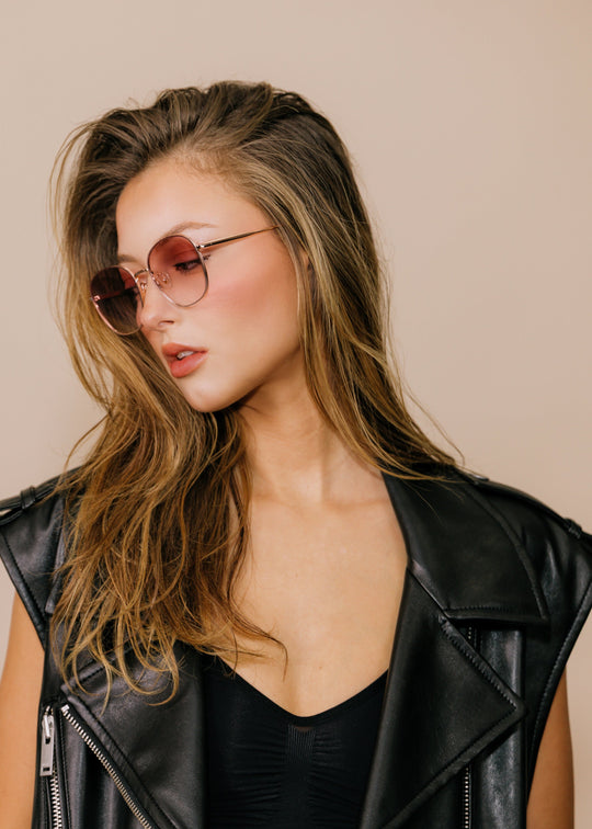 Model wearing Astris sunglasses in Rosé Dawn in three-quarter view, showing the slim rose gold temples and blush lens gradient. 