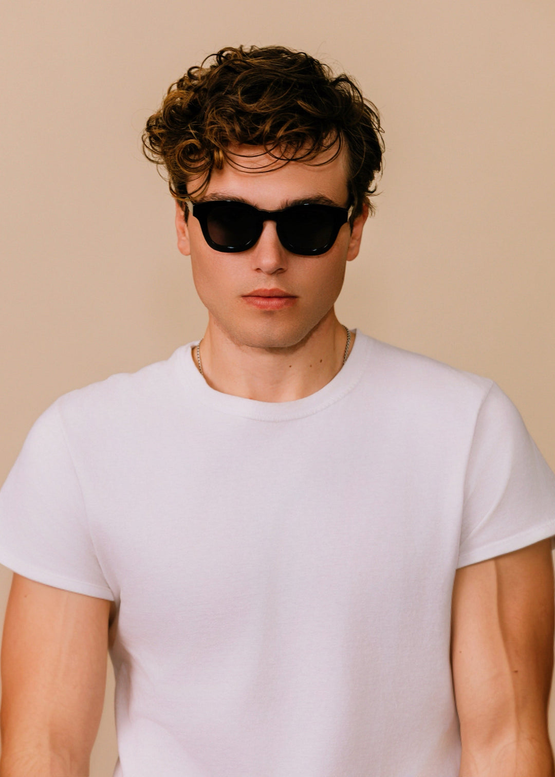 Man wearing black sunglasses and a white t-shirt against a beige background 