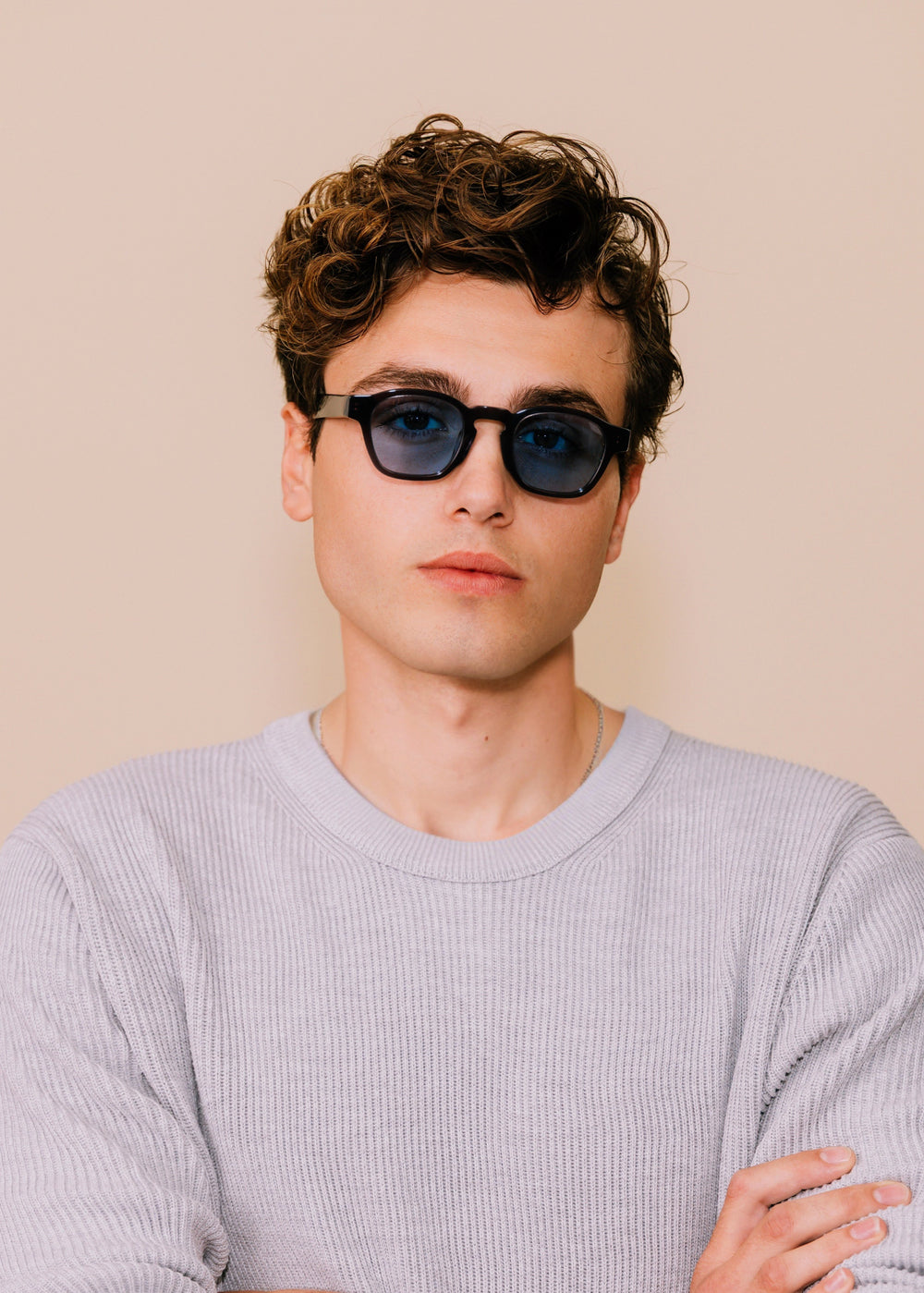 Man wearing sunglasses and a light gray sweater against a beige background