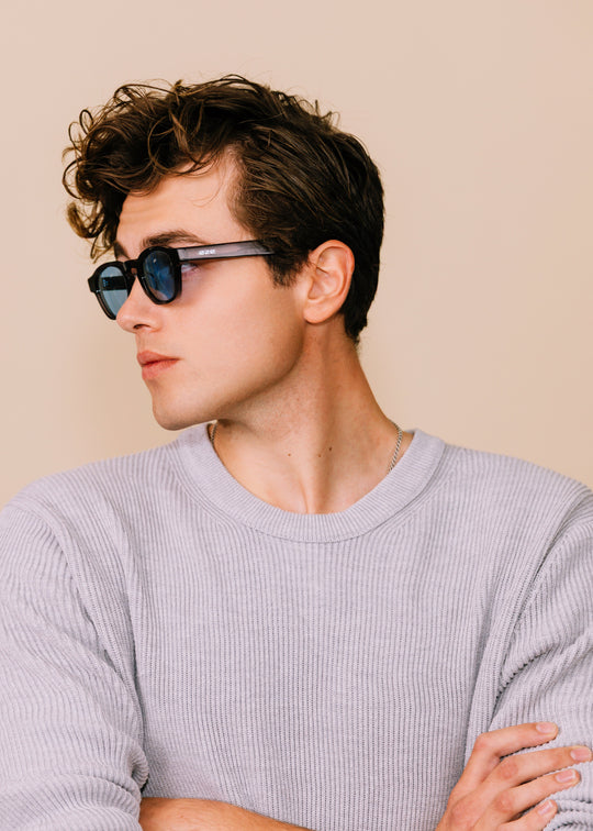 Man wearing sunglasses and a light gray sweater against a beige background