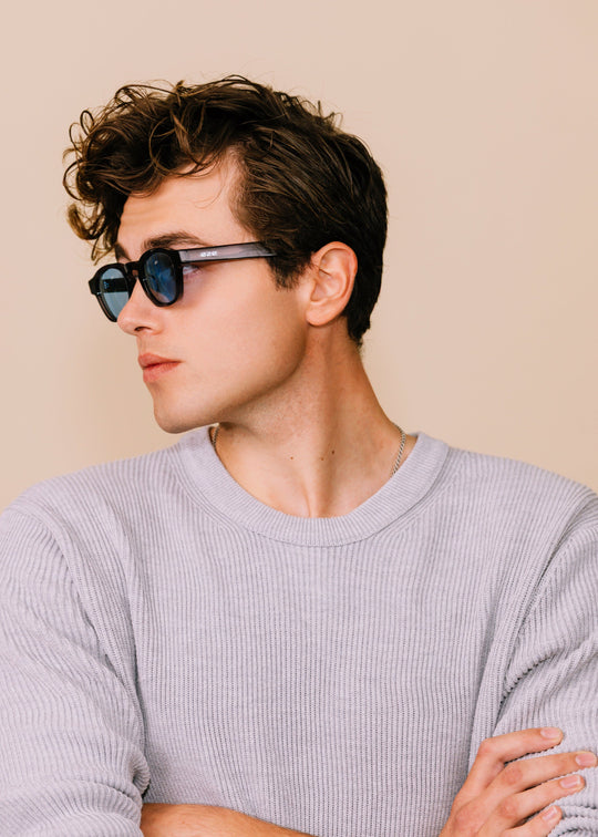 Three-quarter profile portrait of a man wearing Auren sunglasses in Mahogany Smoke with a light gray sweater. 