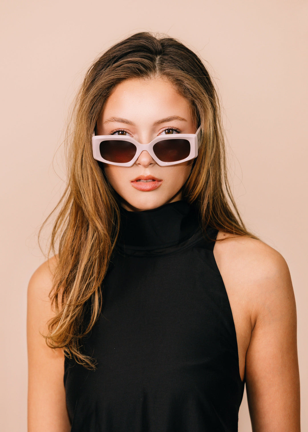 Woman wearing sunglasses and a black sleeveless top against a beige background 