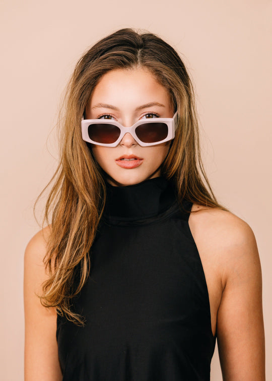 Woman wearing sunglasses and a black sleeveless top against a beige background 