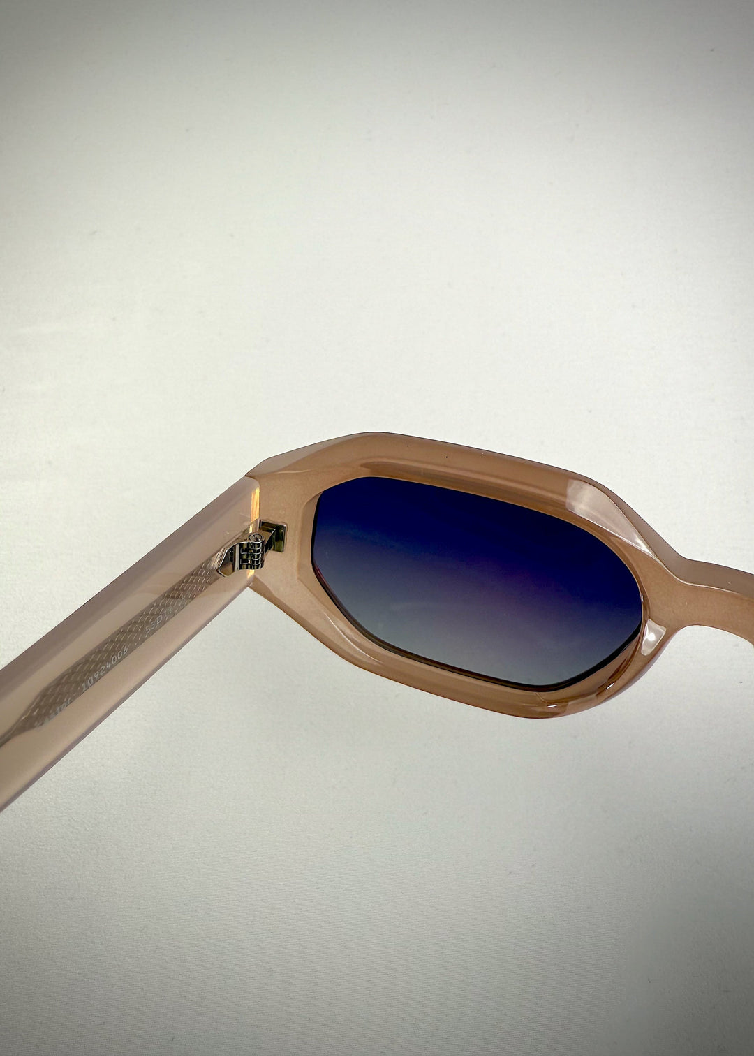 Close-up of Castor Champagne sunglasses – detailed view of acetate frame, metal hinge, and gradient blue lenses. 