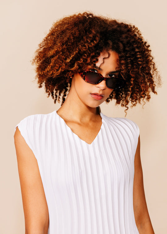 Female model wearing Castor sunglasses in Tortoiseshell, showing the patterned acetate frame and warm brown lenses. 