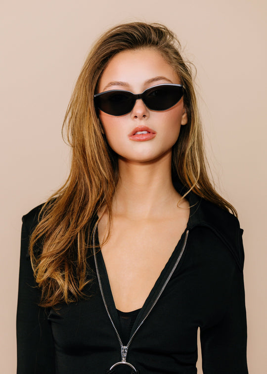Model wearing Celestia – Matte Black, worn low on the nose to show the slim metal browline and wide angular lens shape. 