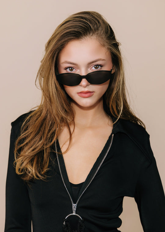 Model wearing Celestia – Matte Black with a black outfit, showing how the wide semi-rimless front sits across the face. 