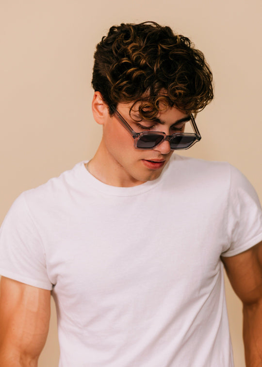 Person wearing a white t-shirt and sunglasses against a beige background 