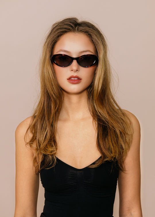 Woman wearing sunglasses and a black dress against a beige background