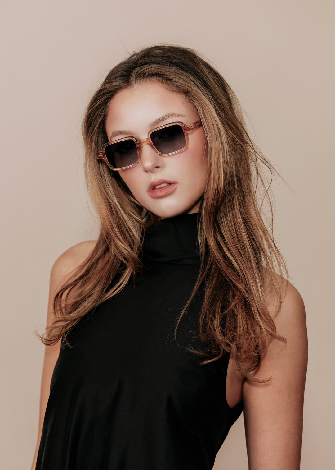 Woman wearing sunglasses and a black outfit against a beige background 