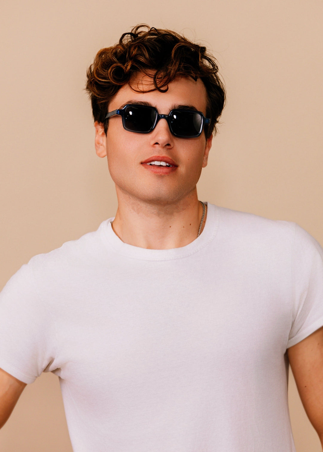 Man wearing sunglasses and a white t-shirt against a beige background 