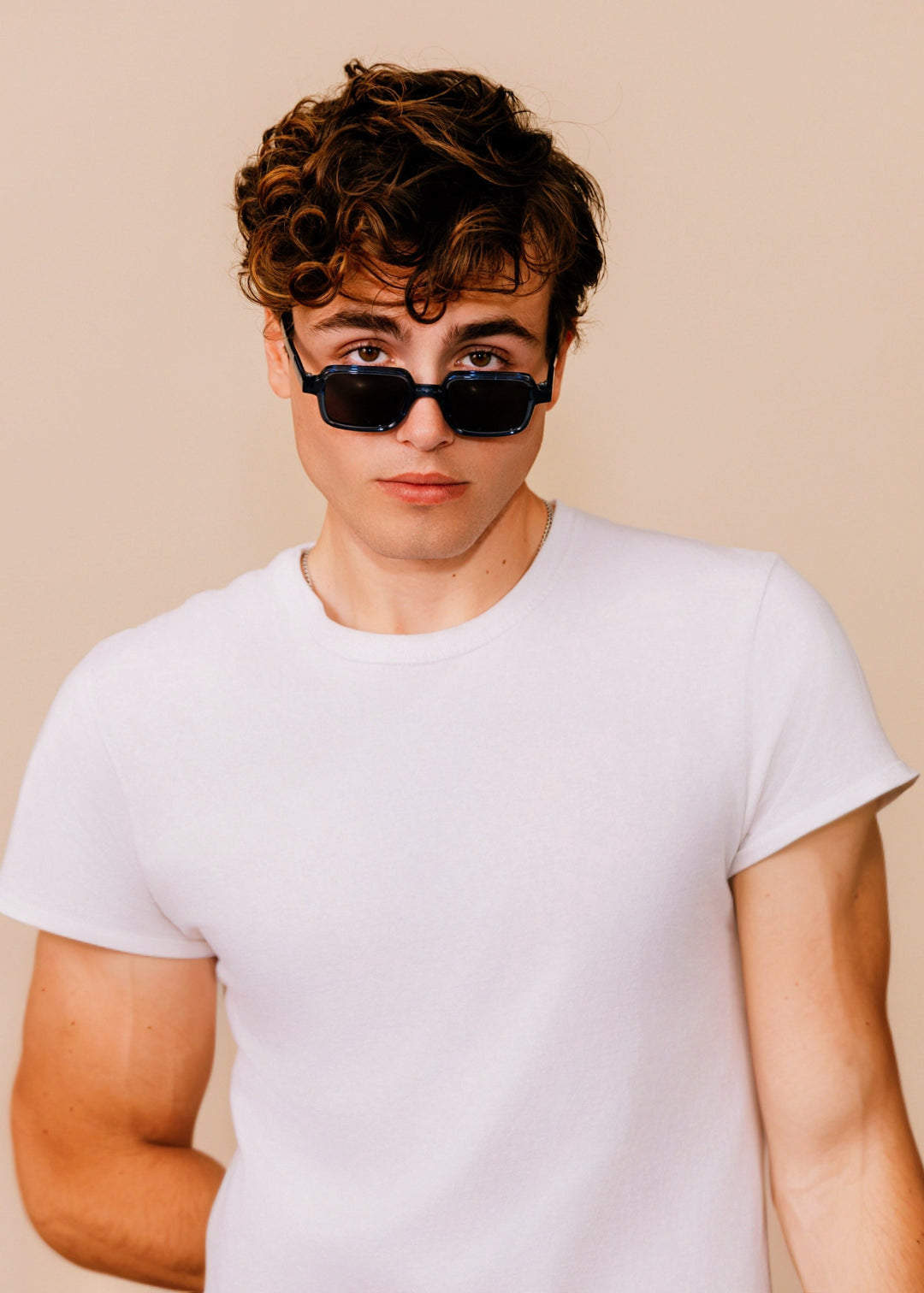 Person wearing sunglasses and a white t-shirt against a beige background 