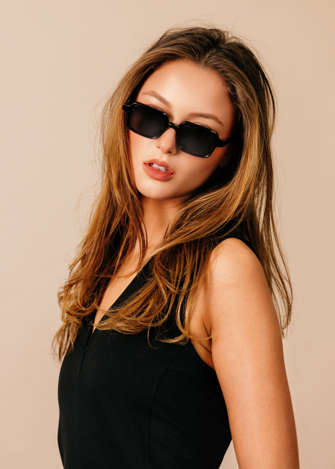 Woman wearing black sunglasses and a black outfit against a beige background 