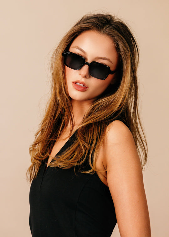 Woman wearing black sunglasses and a black outfit against a beige background 
