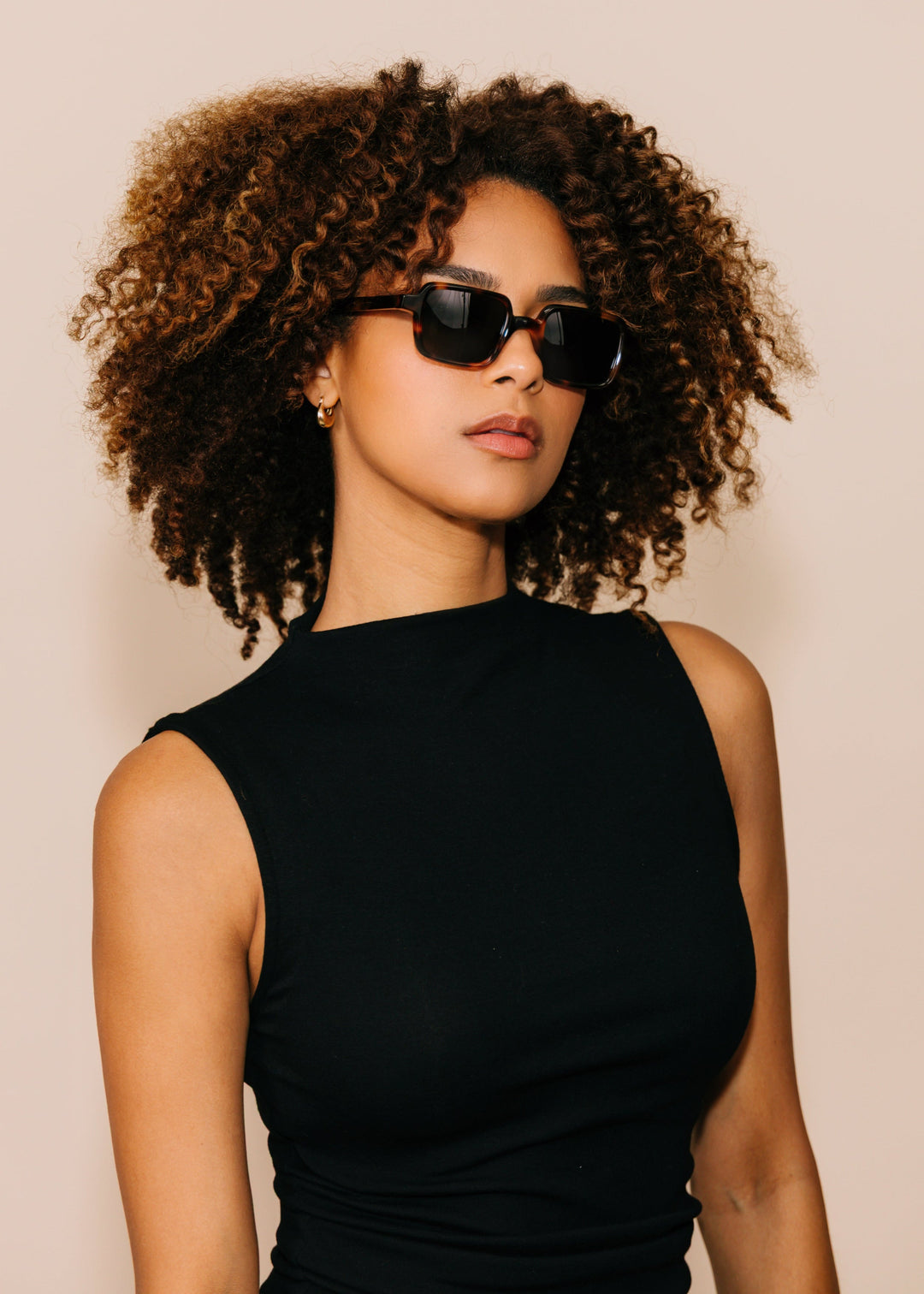 Woman wearing sunglasses and a black dress against a beige background 