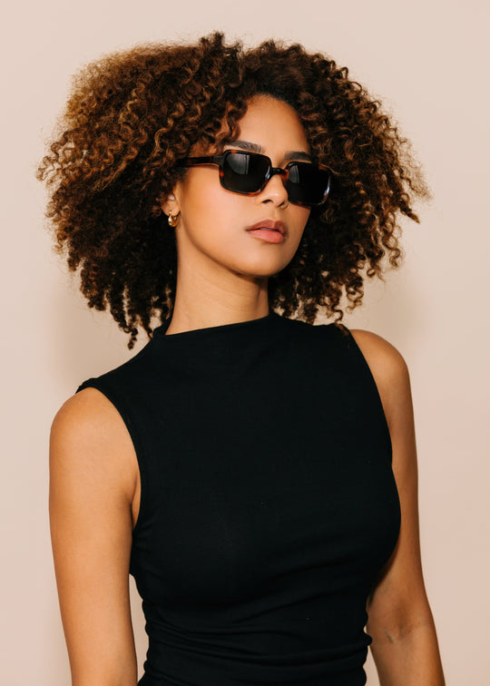 Woman wearing sunglasses and a black dress against a beige background 