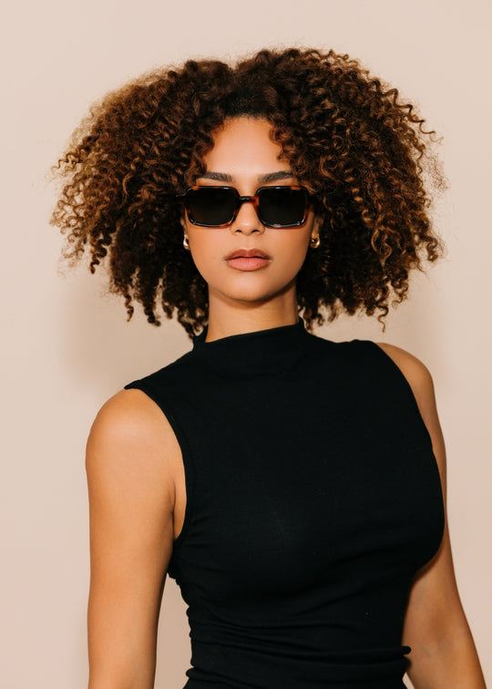Woman wearing sunglasses and a black sleeveless top against a beige background 