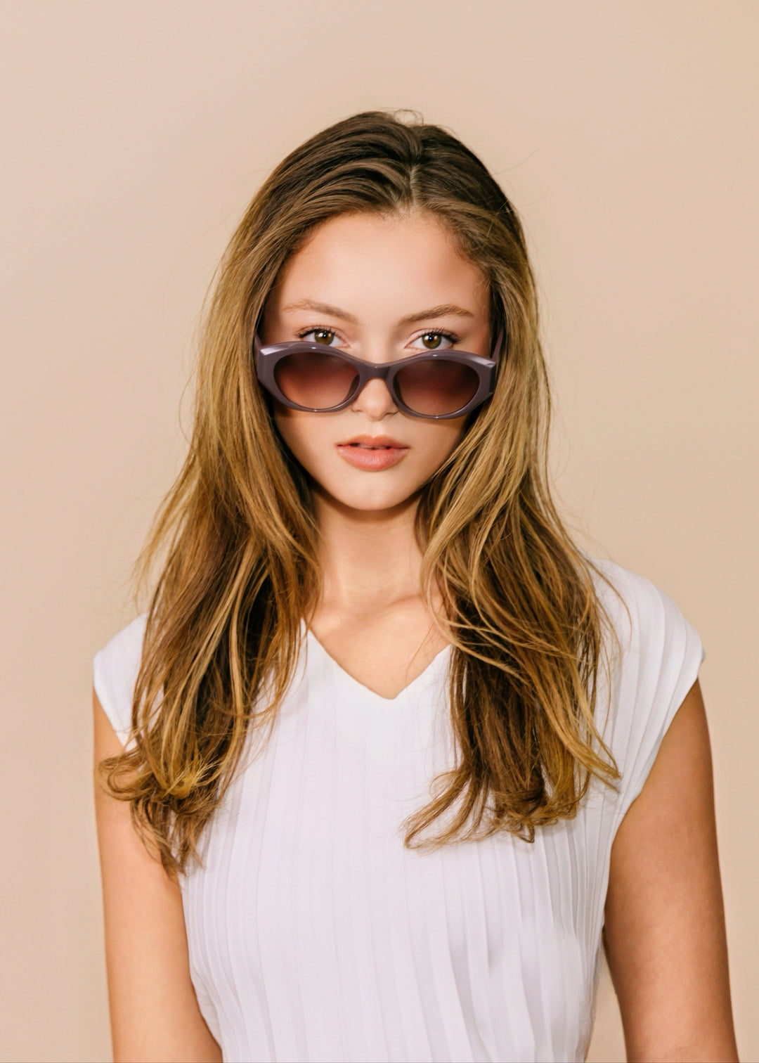 Three-quarter portrait of a model wearing Eclipse Feline sunglasses in Twilight Plum with a white top against a neutral beige background. 
