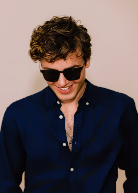 Man wearing sunglasses and a dark blue shirt against a beige background