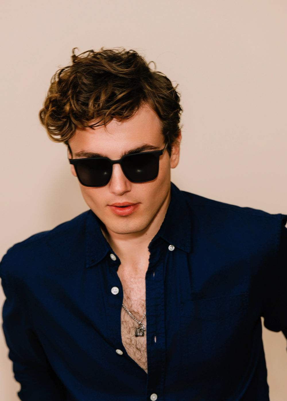 Man wearing sunglasses and a dark blue shirt against a beige background