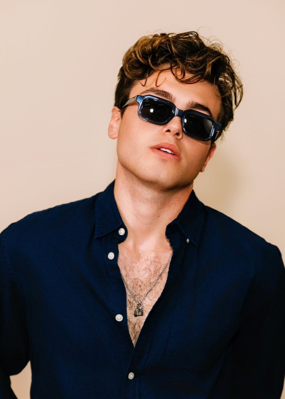 Man wearing sunglasses and a dark shirt against a beige background
