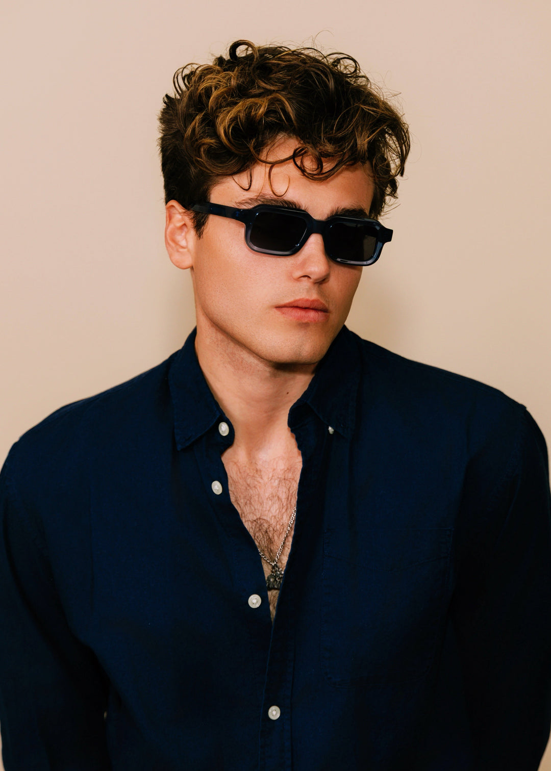 Man wearing sunglasses and a dark shirt against a beige background
