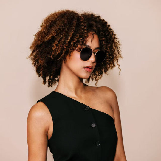 Model wearing Astris sunglasses in Midnight Blue, turned in three-quarter view to show the rose gold frame and deep navy lenses. 