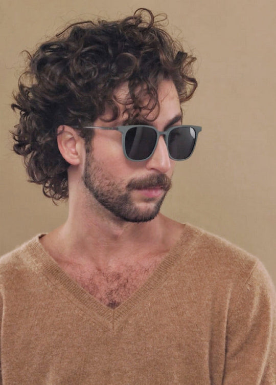 Male model wearing Achernar sunglasses in Deep Matte Green with a tan knit, turned three-quarters. 