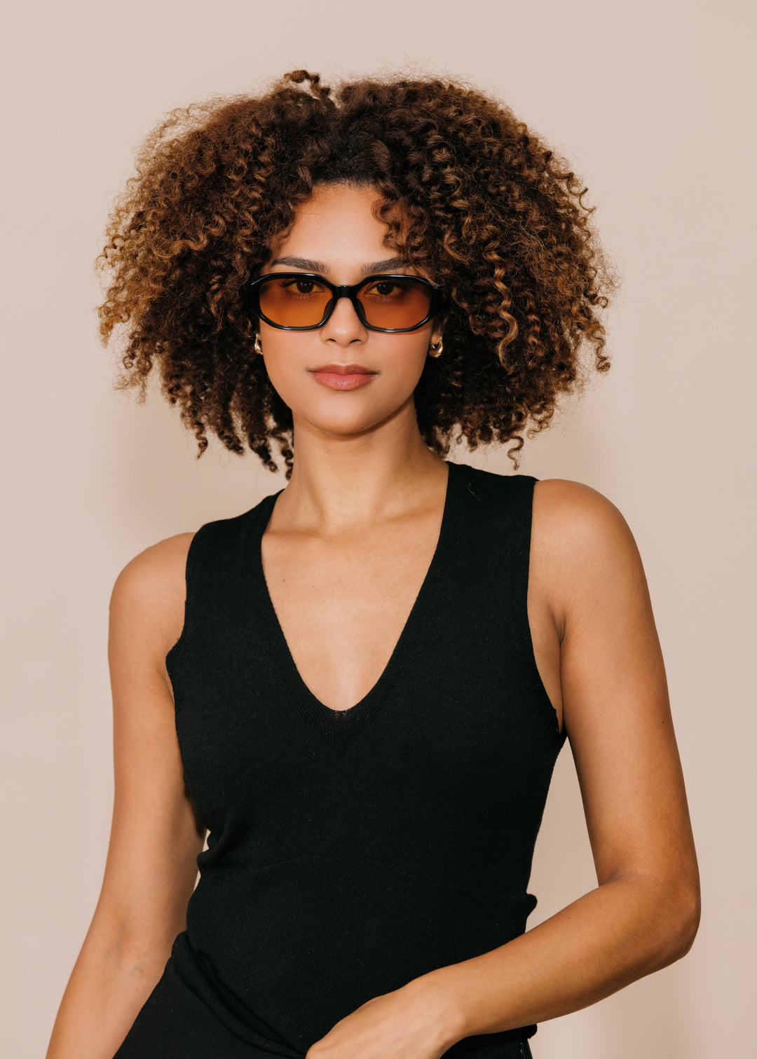 Female model wearing Lyra sunglasses in Amber with a black sleeveless top, facing forward. 