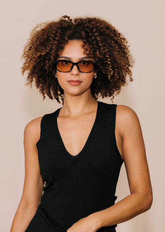 Female model wearing Lyra sunglasses in Amber with a black sleeveless top, facing forward. 