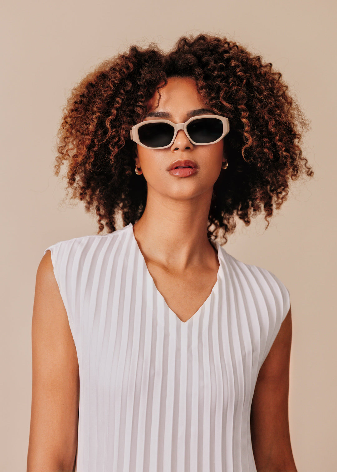 Female model wearing Lyra sunglasses in Creamy Beige with a white pleated top, facing forward. 
