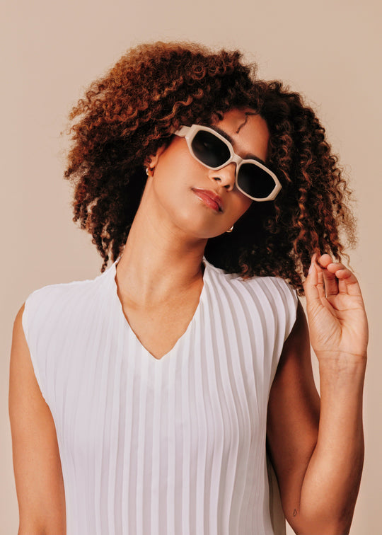 Female model wearing Lyra sunglasses in Creamy Beige against a warm beige backdrop. 