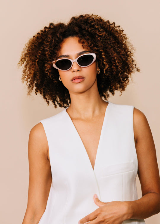 Front portrait of a model wearing Nyx sunglasses in Ash Steel with a white sleeveless top against a neutral beige background. 