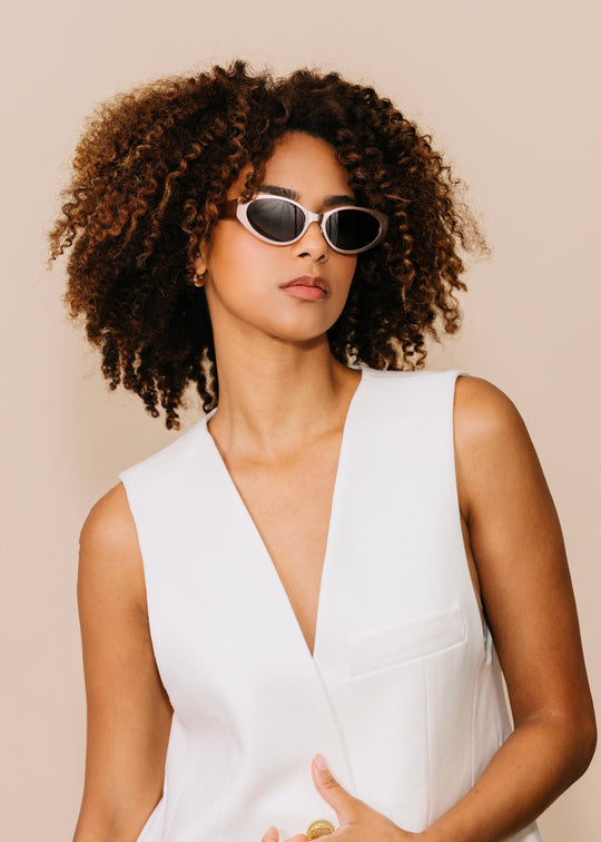 Three-quarter portrait of a model wearing Nyx sunglasses in Ash Steel with a white sleeveless top against a neutral beige background. 