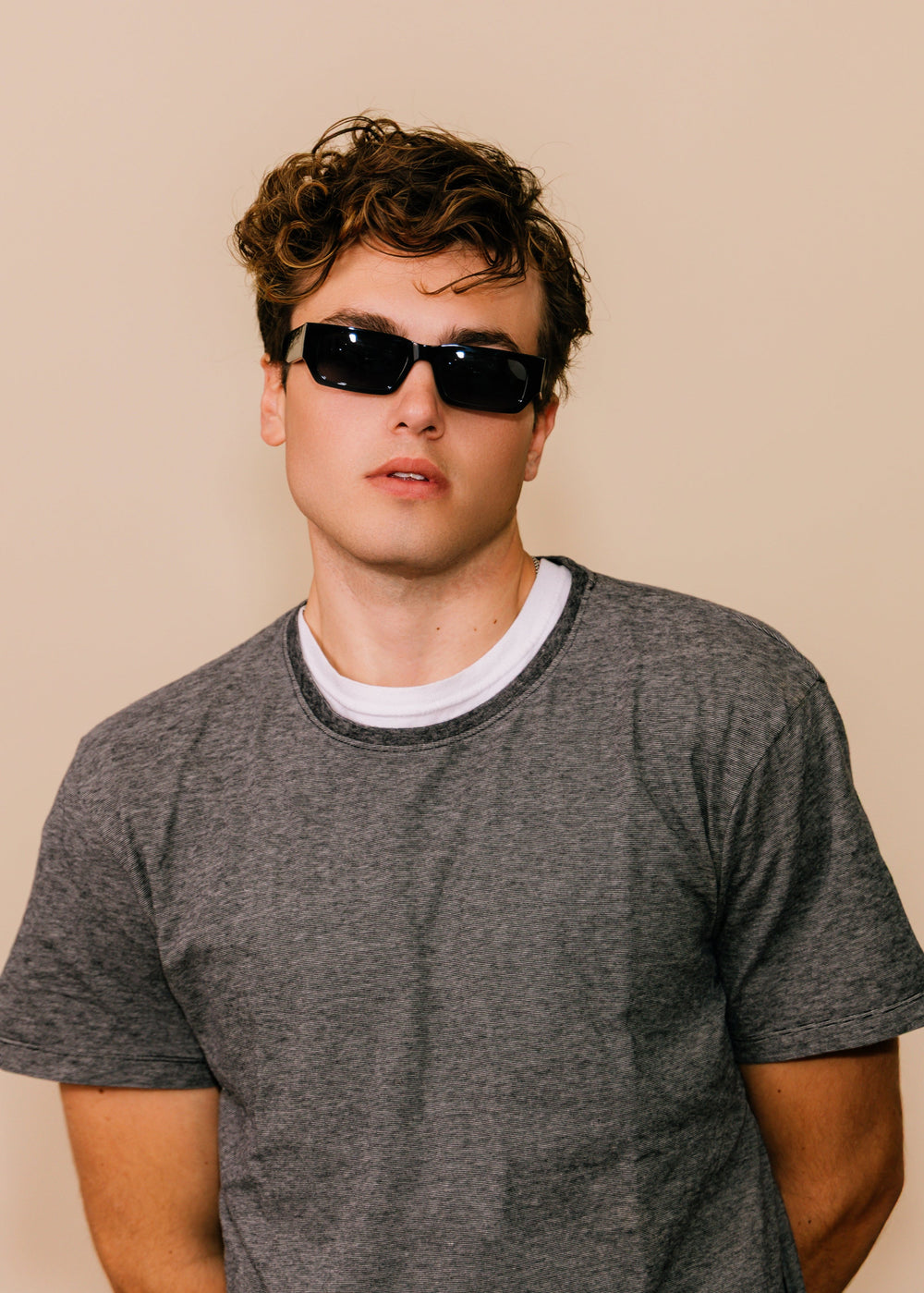 Man wearing sunglasses and a gray t-shirt against a beige background #color_obsidian-black
