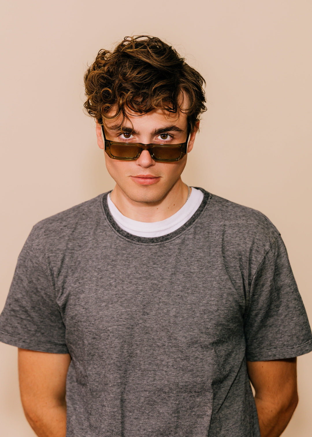 Person wearing sunglasses and a gray t-shirt against a beige background 