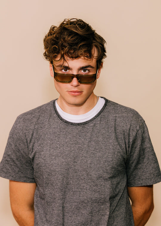 Person wearing sunglasses and a gray t-shirt against a beige background 