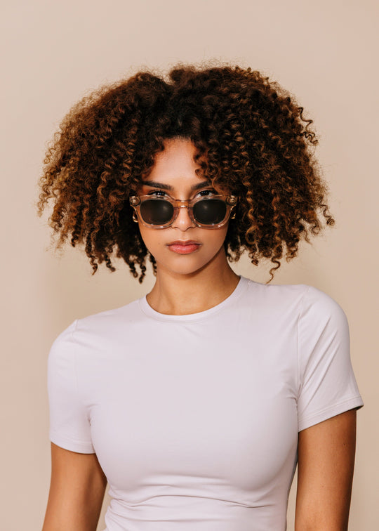 Model wearing Phantom Verge sunglasses in Champagne Moss facing forward, showing how the compact round-oval frame sits on a petite face. 