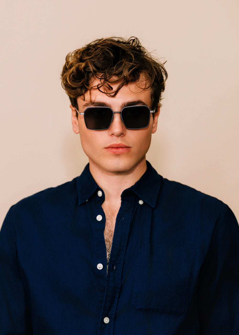 Man wearing sunglasses and a dark blue shirt against a beige background